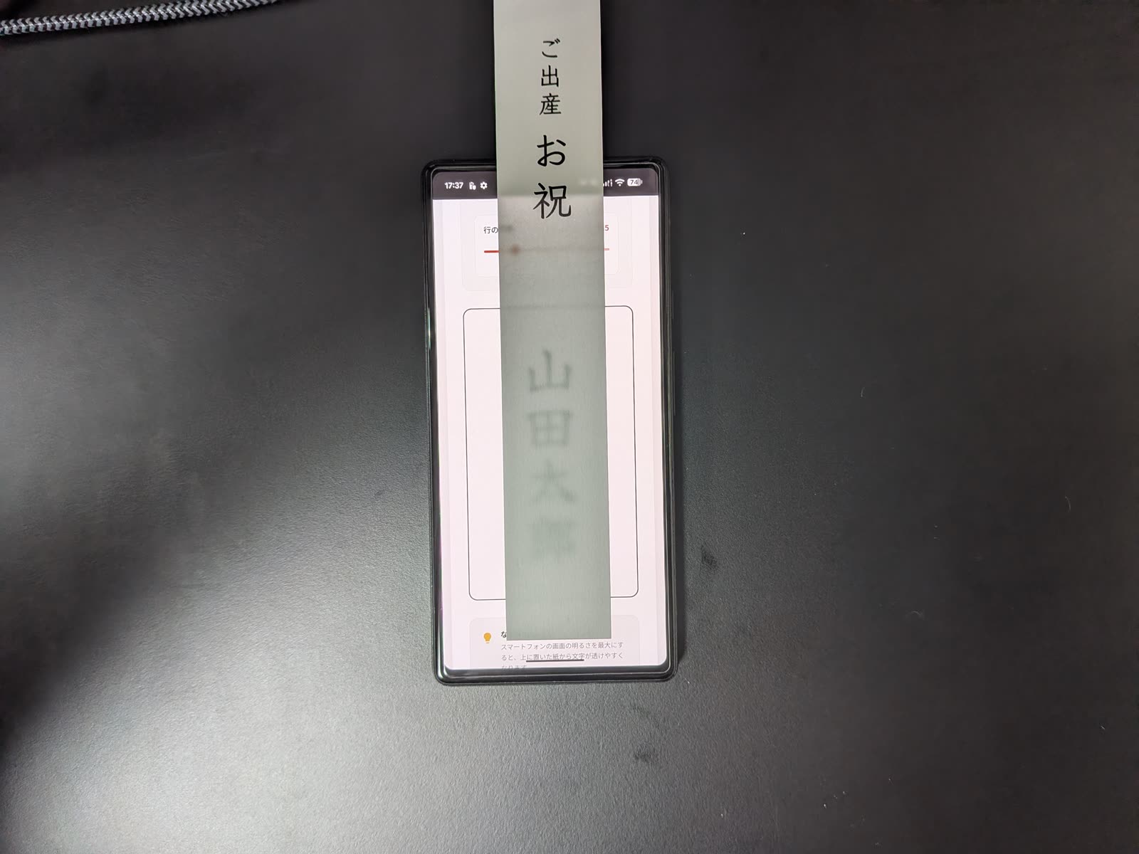 スマートフォンの画面に短冊を重ね、透けて見える「山田太郎」の文字を確認している実物写真